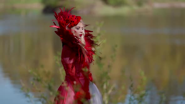 Portrait of a Blonde in a Red Dress with a Feather Collar and a Hat on the Background of a Blurred