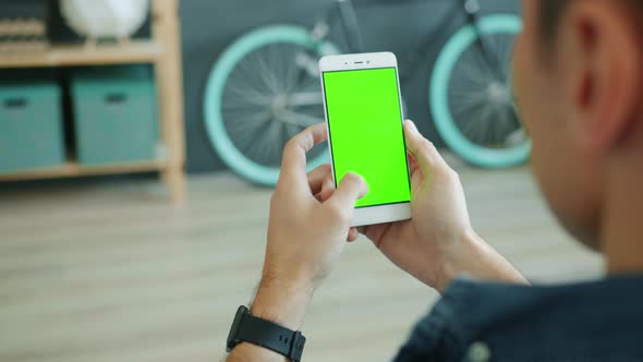 Back View of Man Using Smartphone with Green Chroma Key Screen Holding Modern Device