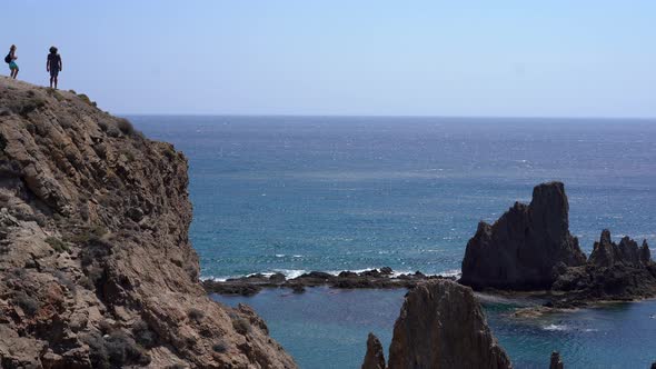 Couple on edge of cliff at Las Sirenas, Cabo De Gata, Almeria. Zoom in