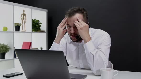 Young Angry Man in Formal Suit and Headphones Working Away From Office at Laptop