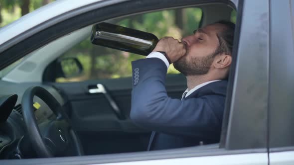 Frustrated Depressed Young Man Sitting in Car Drinking From Bottle Leaning on Steering Wheel