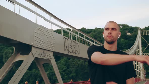 Man Runner in Black Sport Uniform Stretching Hands Before Sports on Pedestrian Bridge at Dawn