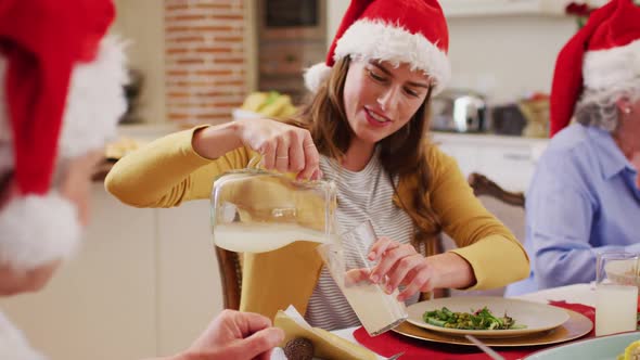 Caucasian woman in santa hat pouring drink in glass of senior man while sitting on dining table and