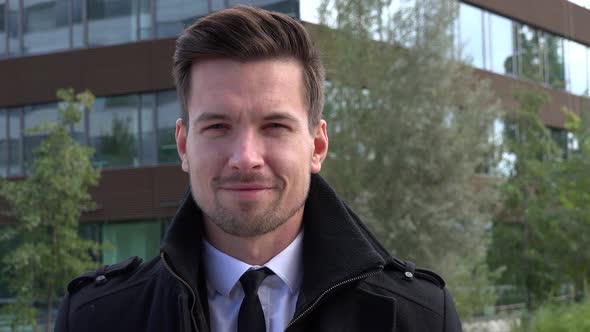 A Young Handsome Man in a Suit Smiles at the Camera - Face Closeup - an Office Building