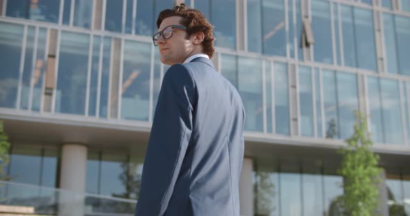 Back View of Serious Businessman in Eye Glasses Looking Up While Standing Against Glass Skyscraper