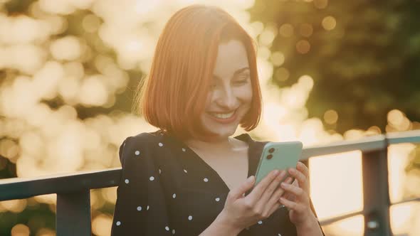 Attractive Redhead Girl Teenager Woman Stands on Street Outdoors Sunlight Rays Sunset Looks in