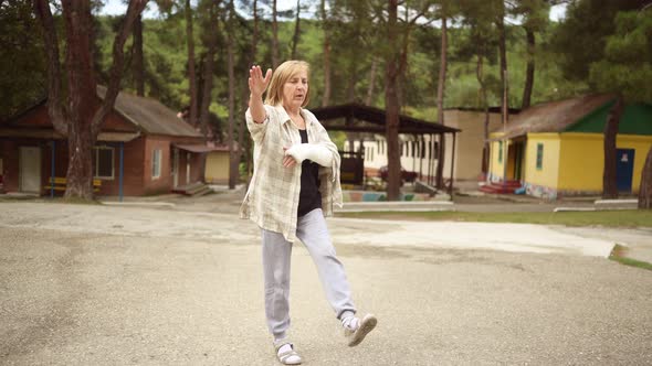 Senior Elderly Woman Doing Exercises and Gymnastic for Hand with Injury Broken Arm in Cast Outside