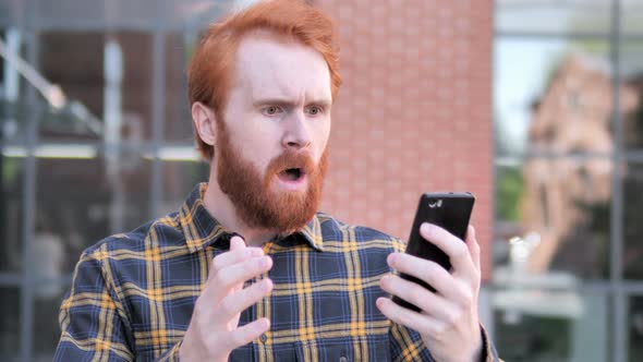 Outdoor Redhead Man Upset by Loss while Using Smartphone