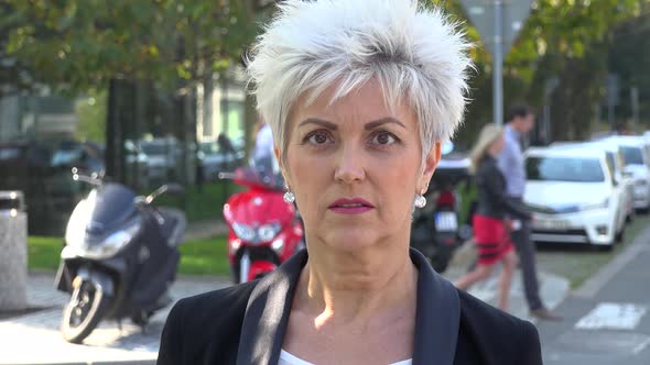 A Middle-aged Woman Looks Seriously at the Camera in a Street in an Urban Area - Closeup