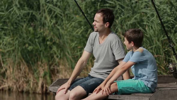 Father and Son Sitting on the Pier and Fishing