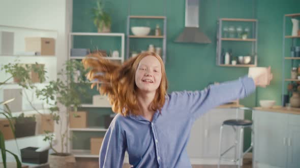 Cute Redhaired Teenage Girl Dancing Vigorously in Modern Kitchen at Home