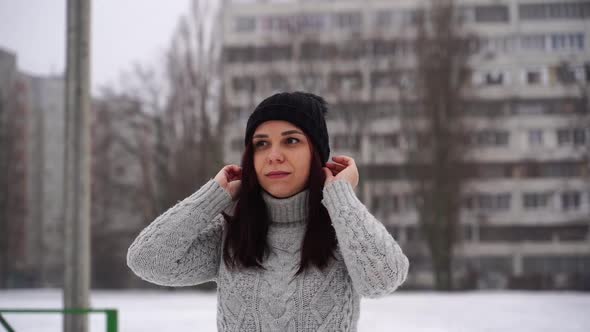Young Woman in Gray Knitted Sweater and Hat Standing on Street in Winter Season