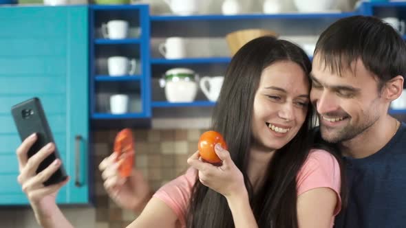 girl covers nose with tomato and her eyes with chopped paprika in the kitchen.