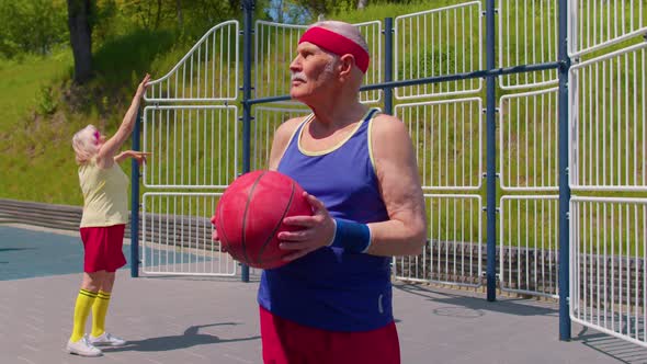 Senior Man Grandfather Posing with Ball Looking at Camera Outdoors on Basketball Playground Court