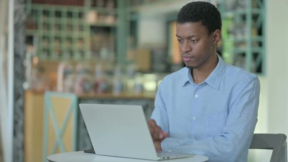 Pensive Young African Man Using Laptop in Cafe