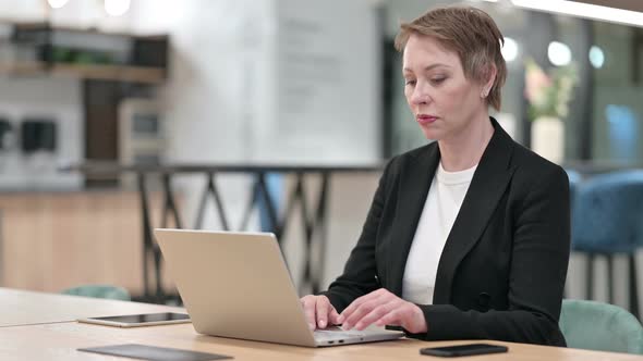 Focused Old Businesswoman Working on Laptop in Office 