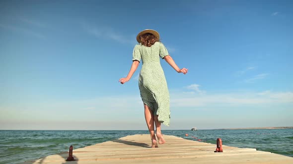 A Young Attractive Slender Caucasian Woman in a Green Dress and a Straw Hat Walks in the Summer