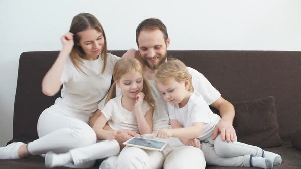 Attractive Happy Family Consisted of Mother Father Son and Daughter Sitting on Sofa at Home 