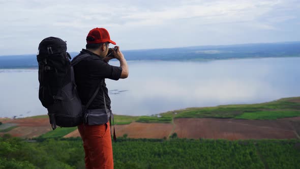 man traveler with backpack using camera taking a photo on the edge of cliff