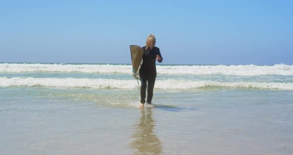 Front view of active senior Caucasian female surfer running on sea in the sunshine 4k