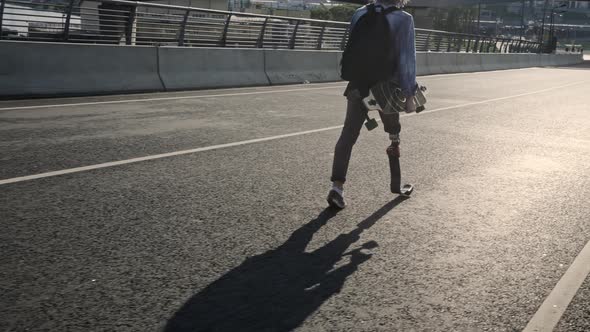 Man with Leg Prosthesis Skateboards Along City Embankment
