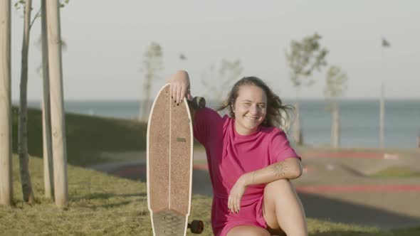 Happy Girl with Skateboard Sitting on Lawn in Skate Park