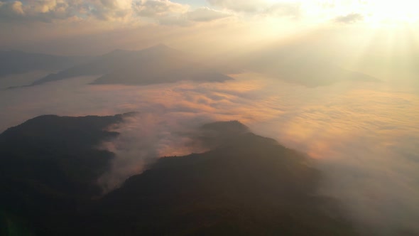 The rays of the sun shine through the clouds into the misty above the mountains in the morning