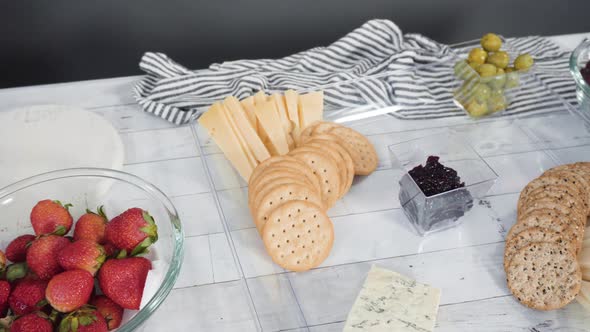 Step by step. Arranging cheese platter with fresh fruits, gourmet cheese, and crackers.