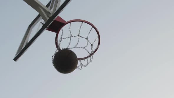 Brown Basketball Ball Fall Through Basket with Metal Chain Net on Sunny Summer Day Close Up