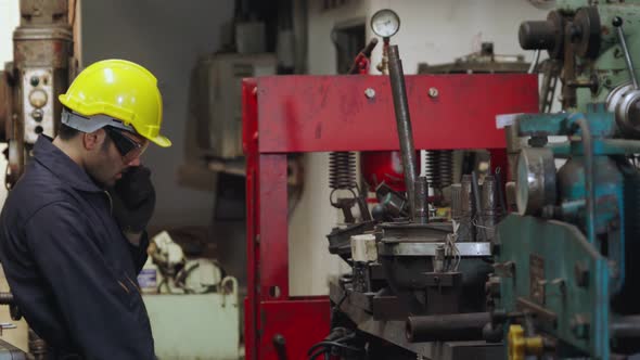 Factory Worker Talking on Portable Radio While Inspecting Machinery Parts