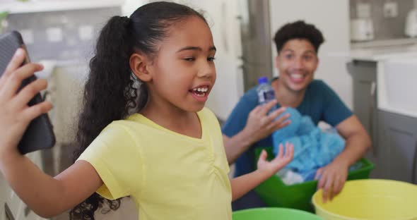 Happy biracial father and daughter making video call using smartphone, sorting waste together