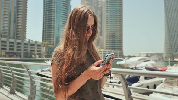 A Girl with Long Hair Dials a Message on the Smartphone at the Quay of Dubai Marina