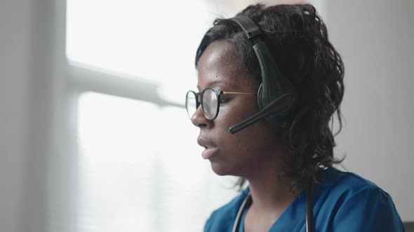 African American Black Female General Practitioner in White Coat Sitting at Desk in Doctor's Office