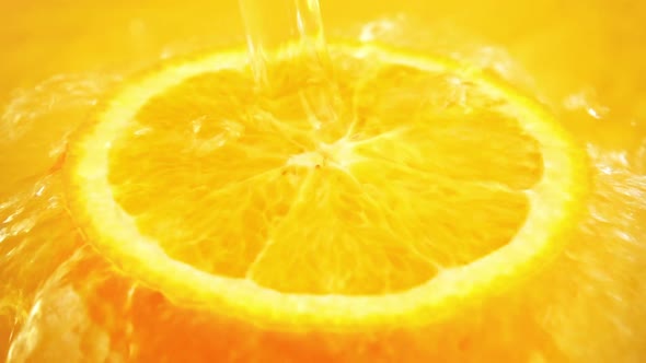 Half of an orange in a jet of water on an orange background. Slow motion.