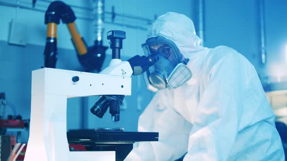 Male Specialist in a Hazmat Suit is Operating a Microscope