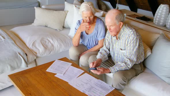 High angle view of old Caucasian senior couple discussing over bills in living room at comfortable h