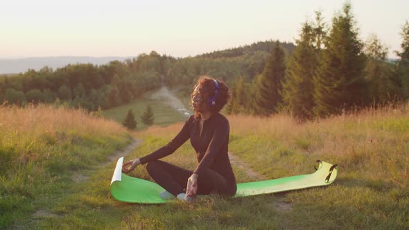 Serene Lovely Black Woman Meditating Listening to Music in Headphones on Mountain Top at Sunrise