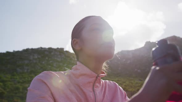 Mixed race woman drinking water while exercising in countryside smiling