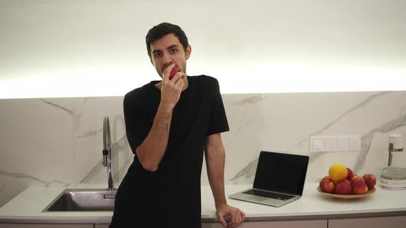 Young Man Eating Red Apple at Home in the Kitchen