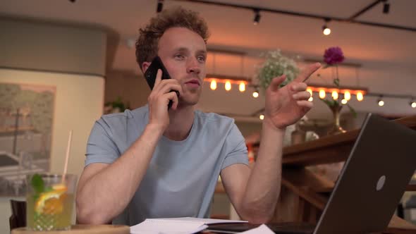 Attractive, young man gesturing with his hands while sitting at a laptop