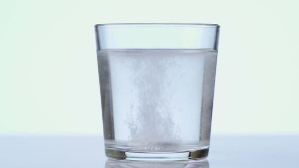 Pill Falling Down in Glass with Water. Effervescent Tablet Aspirin. Closeup on White Background