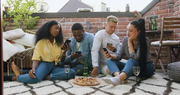 Friends which Sitting on the Carpet in the Balcony and Using thier Smartphones During Summer Party
