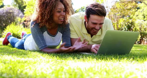 Couple lying on grass and using laptop in park