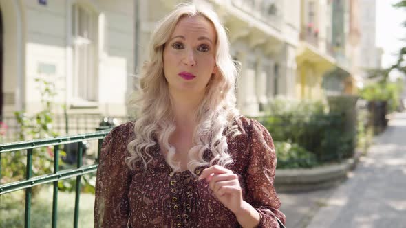 A Middleaged Caucasian Woman Talks to the Camera in an Urban Area  a City Street with Buildings