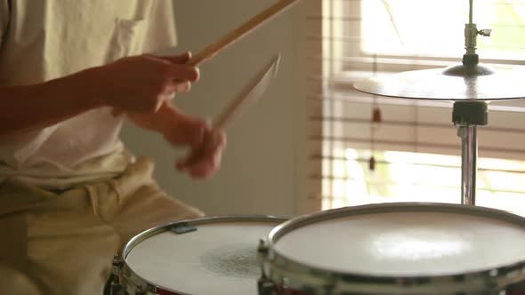 Drummer practicing ghost note rudiments with natural light coming through the window.