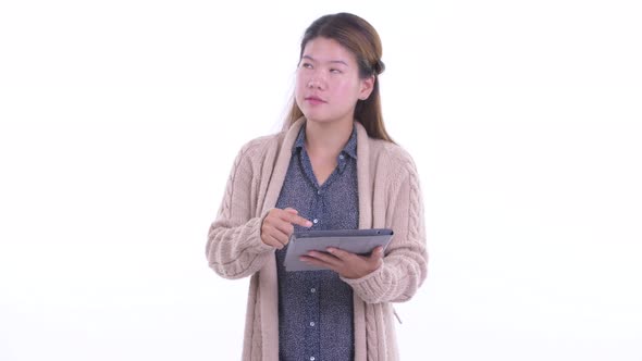 Happy Young Asian Woman Thinking While Using Digital Tablet Ready for Winter