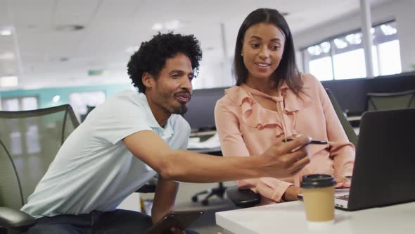 Video of happy diverse businesswoman and businessman using laptop and talking