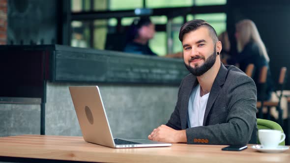 Attractive Smiling Male Businessman Posing Sitting on Table Working Using Laptop at Cafe