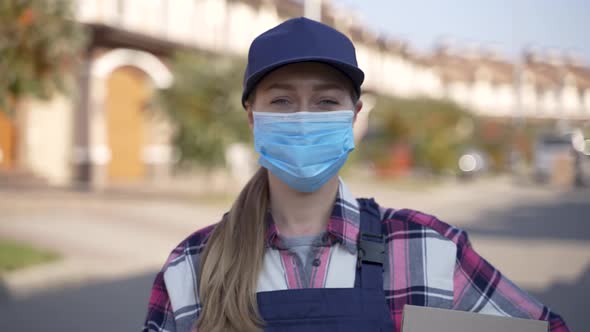 Masked Female Courier Posing with Cardboard Box