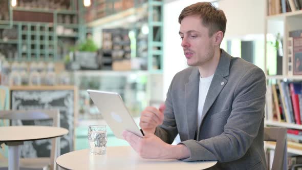 Young Man Making Video Call on Tablet in Cafe